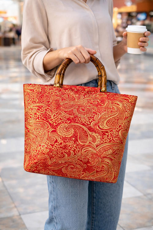 Person holding a red patterned bag and a coffee cup in an outdoor setting