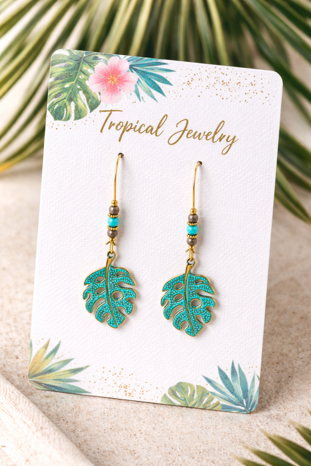 Tropical leaf earrings on a branded card with palm leaves in the background