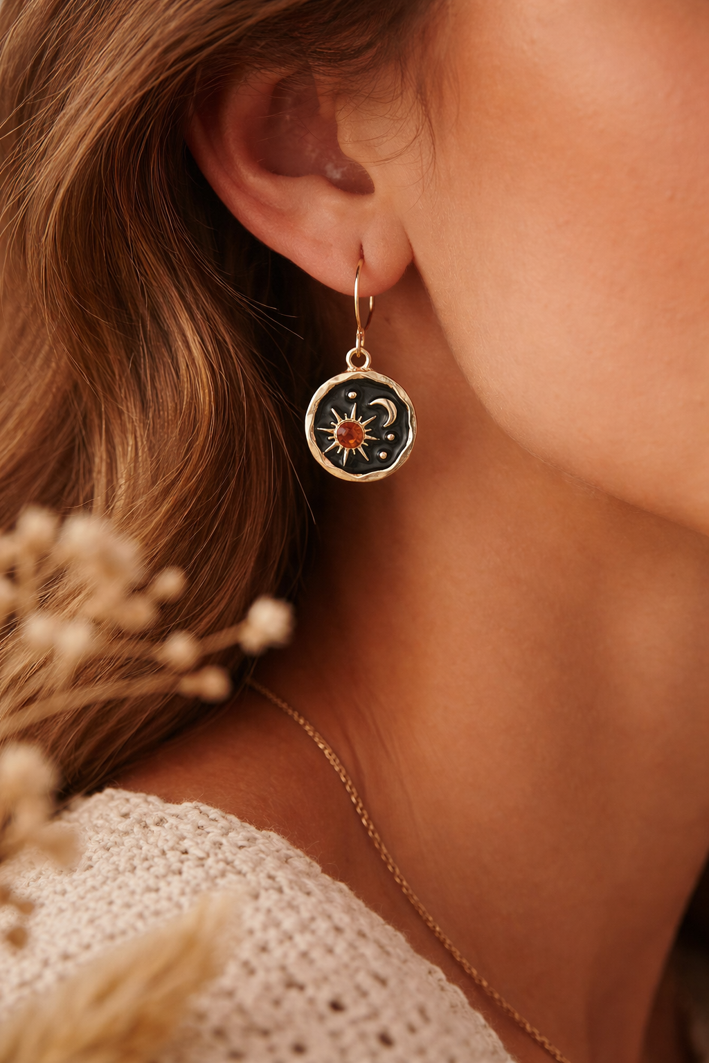 Close-up of a person wearing a gold earring with a circular design, holding dried flowers.