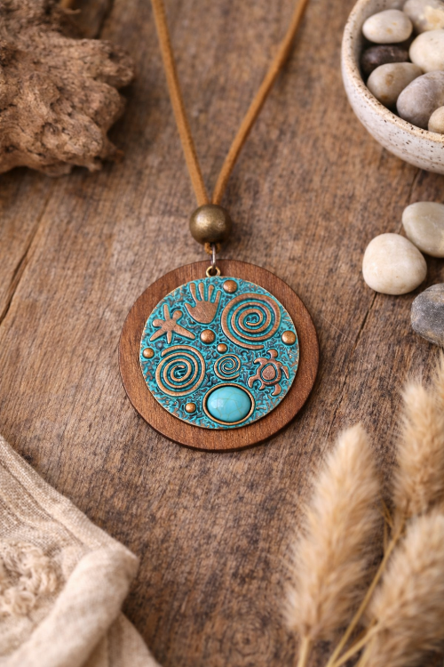 Necklace with a wooden pendant featuring intricate designs on a wooden surface with pebbles and dried plants.