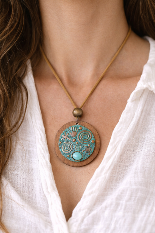 Necklace with a wooden pendant featuring turquoise stones and gold accents on a white shirt.